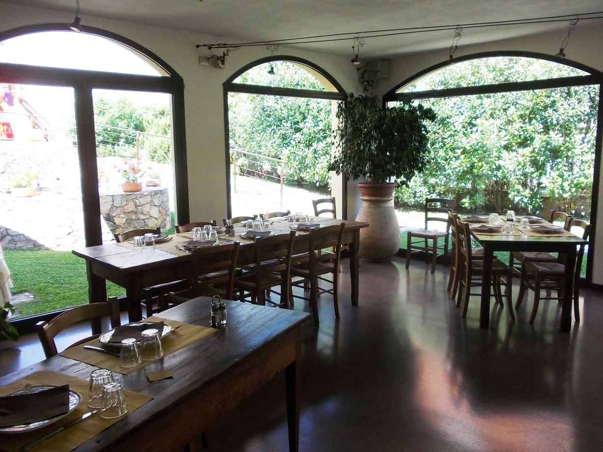 Sala ristorante con tavoli in legno apparecchiati, grandi finestre ad arco sul giardino verde