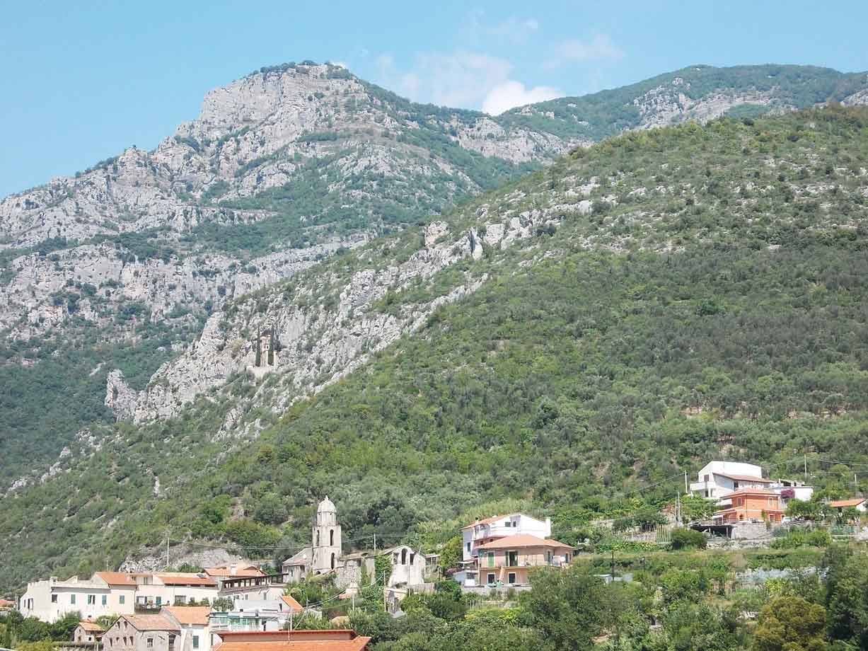 villaggio con campanile tra case e montagna rocciosa verde