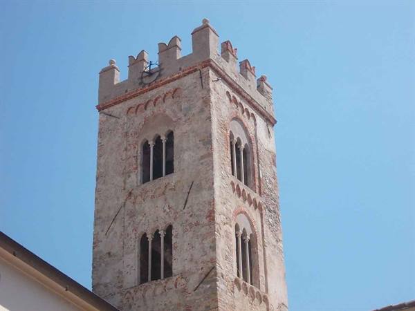 Medieval stone and brick bell tower with mullioned windows and battlements against blue sky