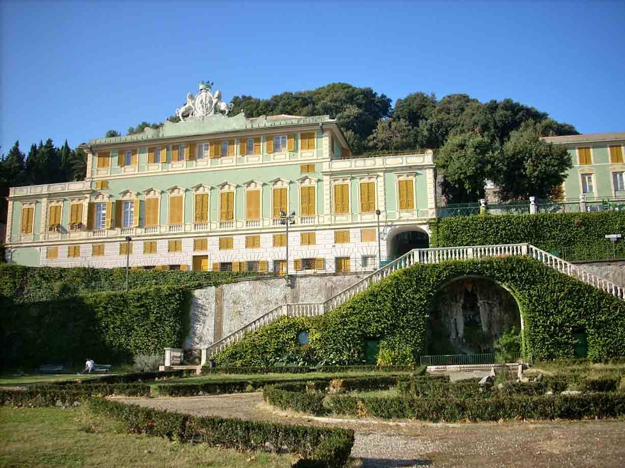 Villa verde con finestre gialle, scalinate in muratura e siepi, cielo azzurro