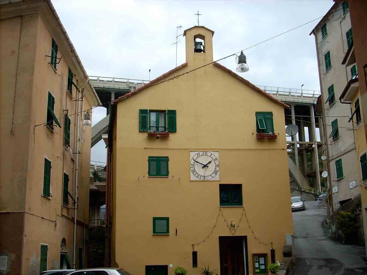 Chiesetta gialla con orologio e campanile, dietro un grande viadotto in cemento
