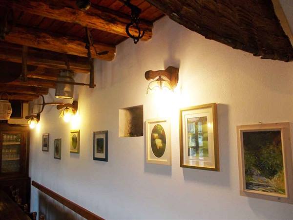 Framed paintings on white wall beneath wooden beams and glowing lamps