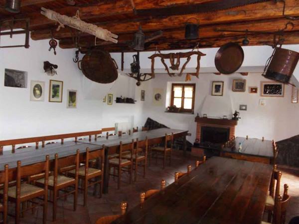 Rustic dining hall with wooden tables, beams and old farm tools hanging from ceiling
