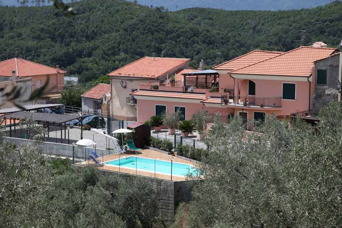 Case rosa con tetti in terracotta e piscina tra gli ulivi sui colli