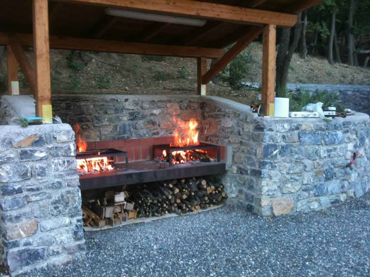 Griglia in pietra con brace accesa sotto tettoia di legno