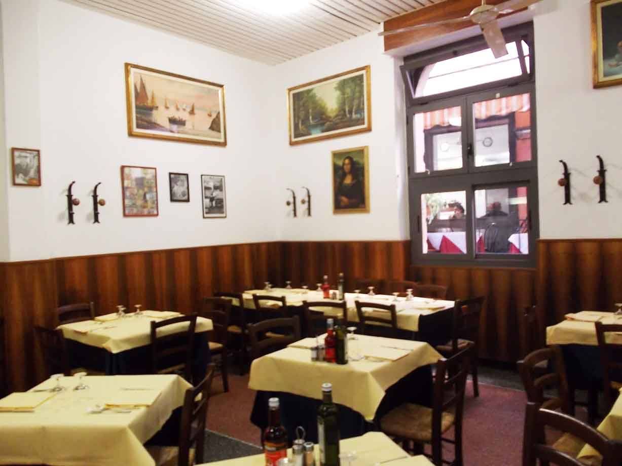 Sala di trattoria con tavoli apparecchiati a tovaglia gialla, quadri e copia della Gioconda alle pareti