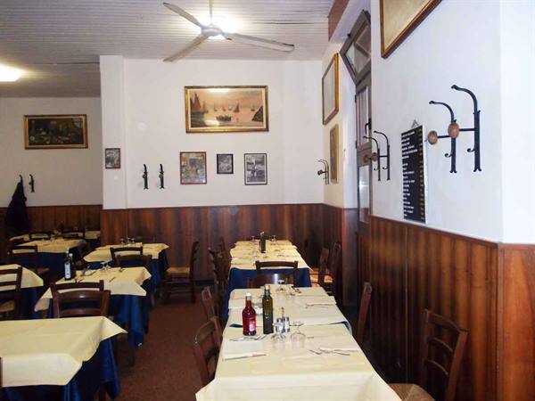 Trattoria dining room with white-clothed tables, wooden chairs and framed pictures on walls
