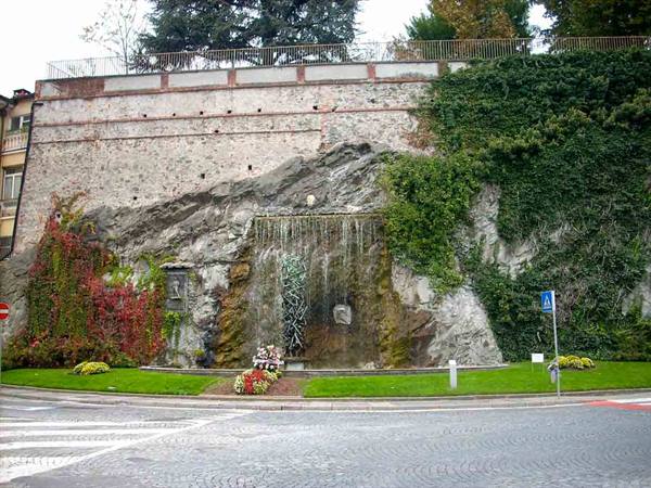 Artificial waterfall on rocky wall with ivy, flowerbeds and old wall above