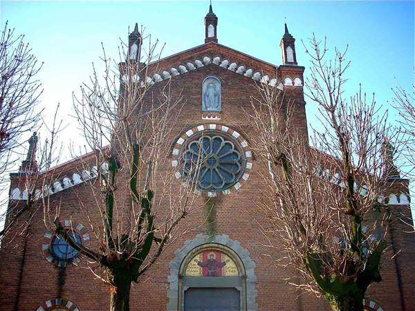 Brick church with rose window and bare trees under blue sky