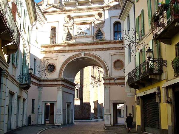 Historic brick arch between balconied buildings, a woman walks through the narrow street