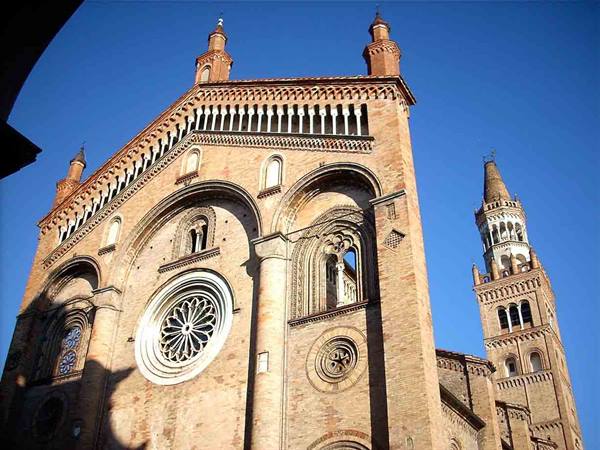 Cremona Cathedral brick facade with rose window and Torrazzo tower under blue sky