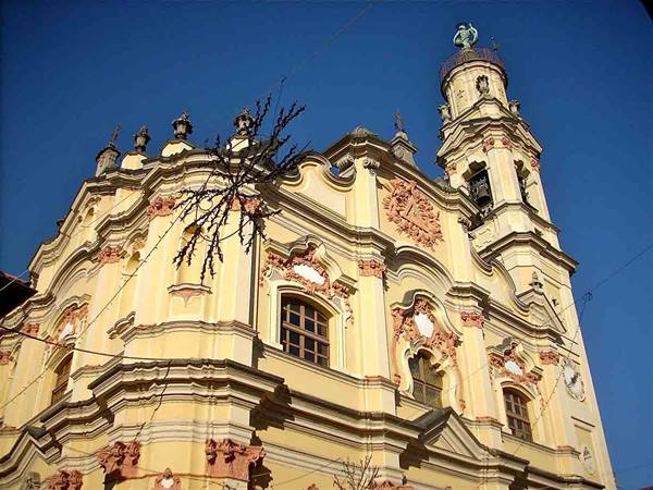 Baroque church in yellow and pink against blue sky, copper statue tower