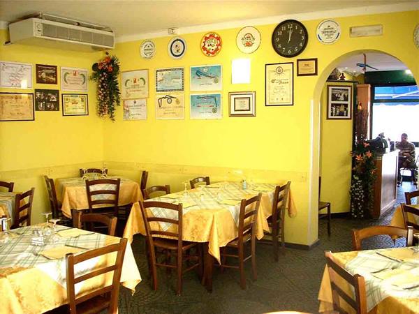 Trattoria dining room with set tables, wooden chairs, yellow walls and framed certificates