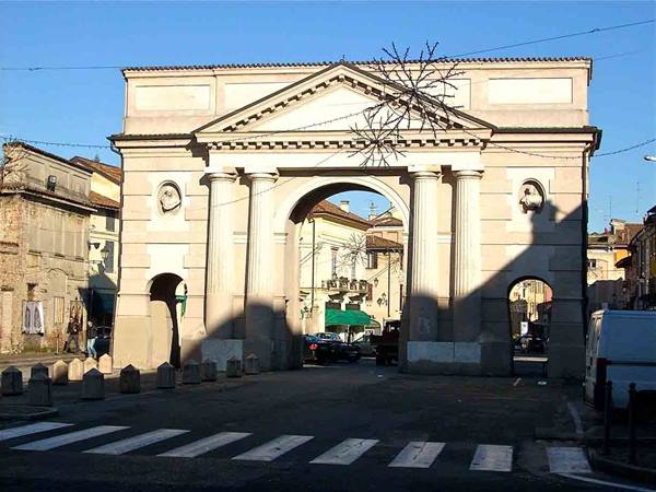 Neoclassical stone gate with columns and pediment, sunlight on town buildings