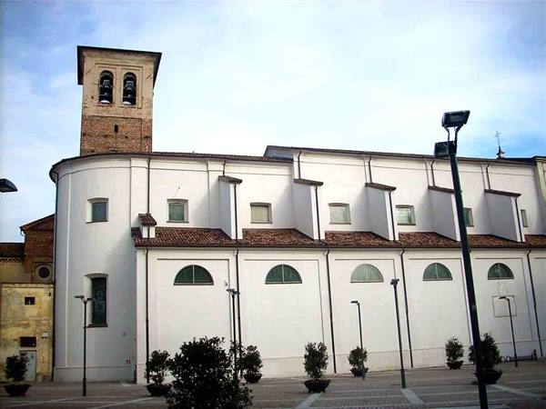 White church with brick bell tower and buttresses, square with plant pots