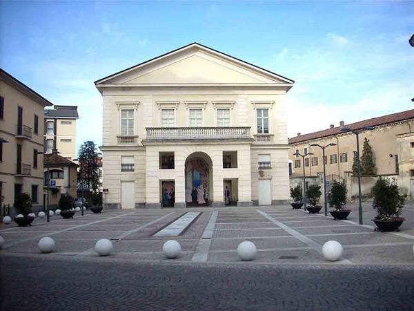 White neoclassical theater with pediment and arch, stone square with marble spheres