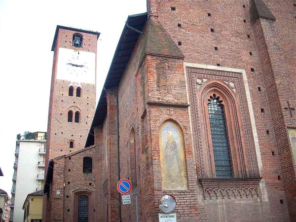 Brick bell tower with clock and church wall with faded fresco