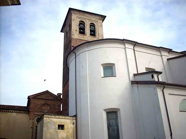 Brick bell tower with bells and white church apse under cloudy sky