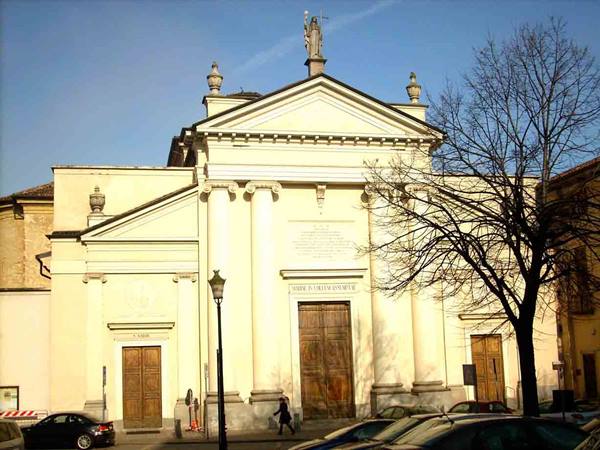 Yellow neoclassical church with statues on the pediment, parked cars below