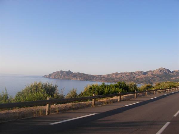 Coastal road with wooden guardrail, blue sea and rocky mountains under clear sky