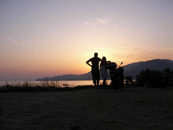 Couple in silhouette beside a scooter watching the sea at dusk