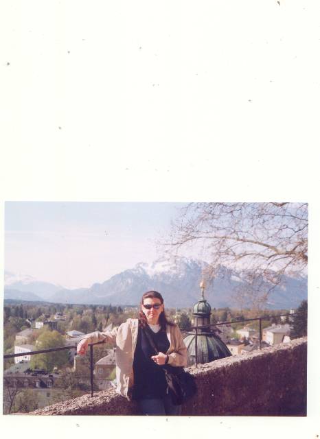 Woman leaning on stone wall, green dome and snowy mountains, Salzburg