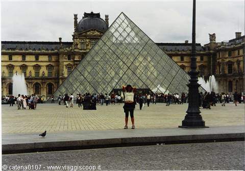 Tourist photographs the Louvre glass pyramid among fountains and visitors