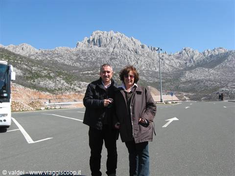 Smiling couple in a parking lot before the rocky Velebit peaks, bright light