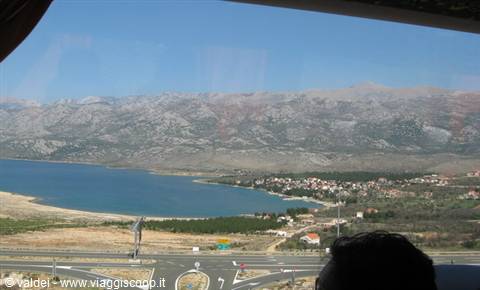 Turquoise bay beneath rocky mountains, coastal village seen from the bus