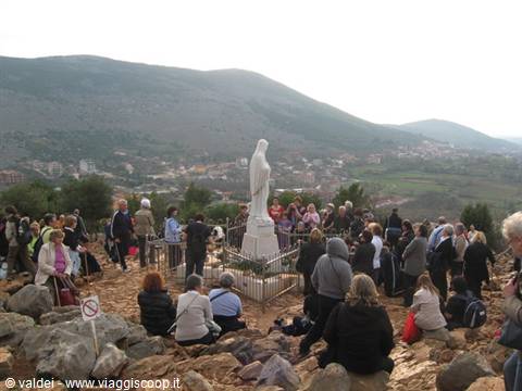Pilgrims praying around the white Virgin Mary statue on Apparition Hill, Medjugorje