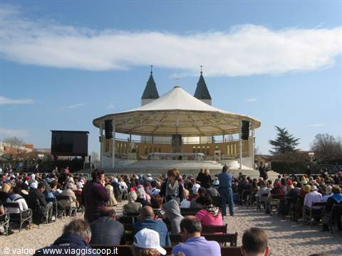 Crowd gathered before Medjugorje's open-air altar, white canopy and green spires behind