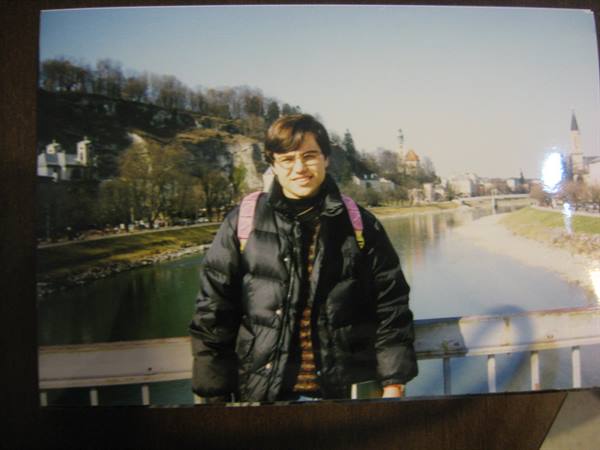 Boy in black down jacket with pink backpack on Salzburg bridge over Salzach