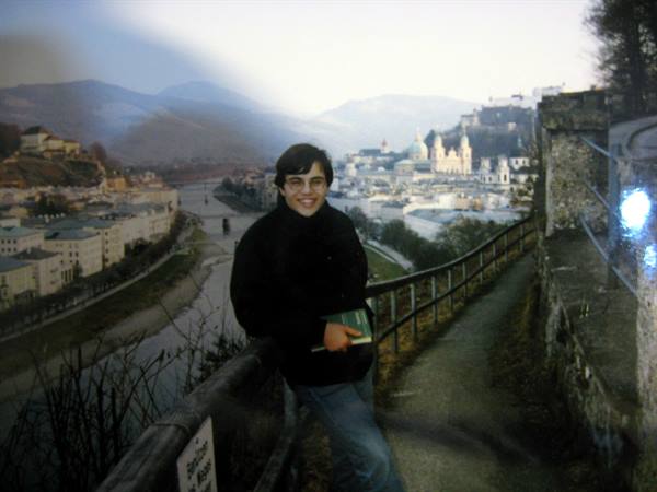 Smiling young man holding a book on a path above Salzburg, domes and river below