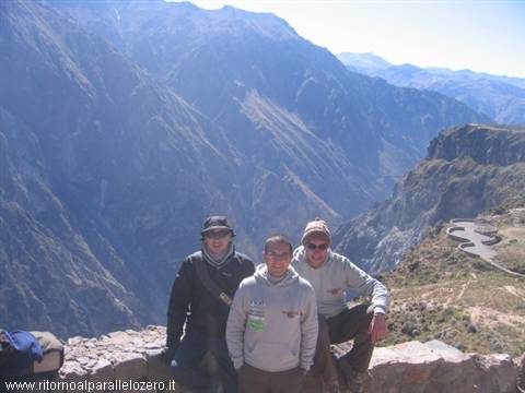 Three tourists on a stone wall above Colca Canyon