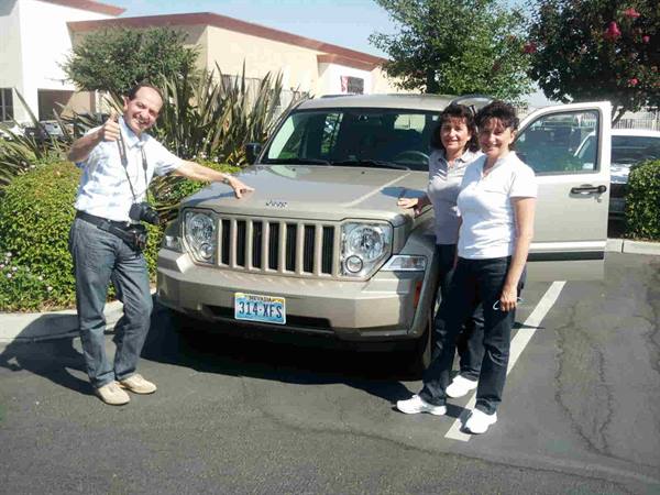 Three people beside a gold Jeep in a sunny parking lot