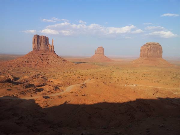 Monument Valley: red sandstone buttes over the desert, dirt road, afternoon light
