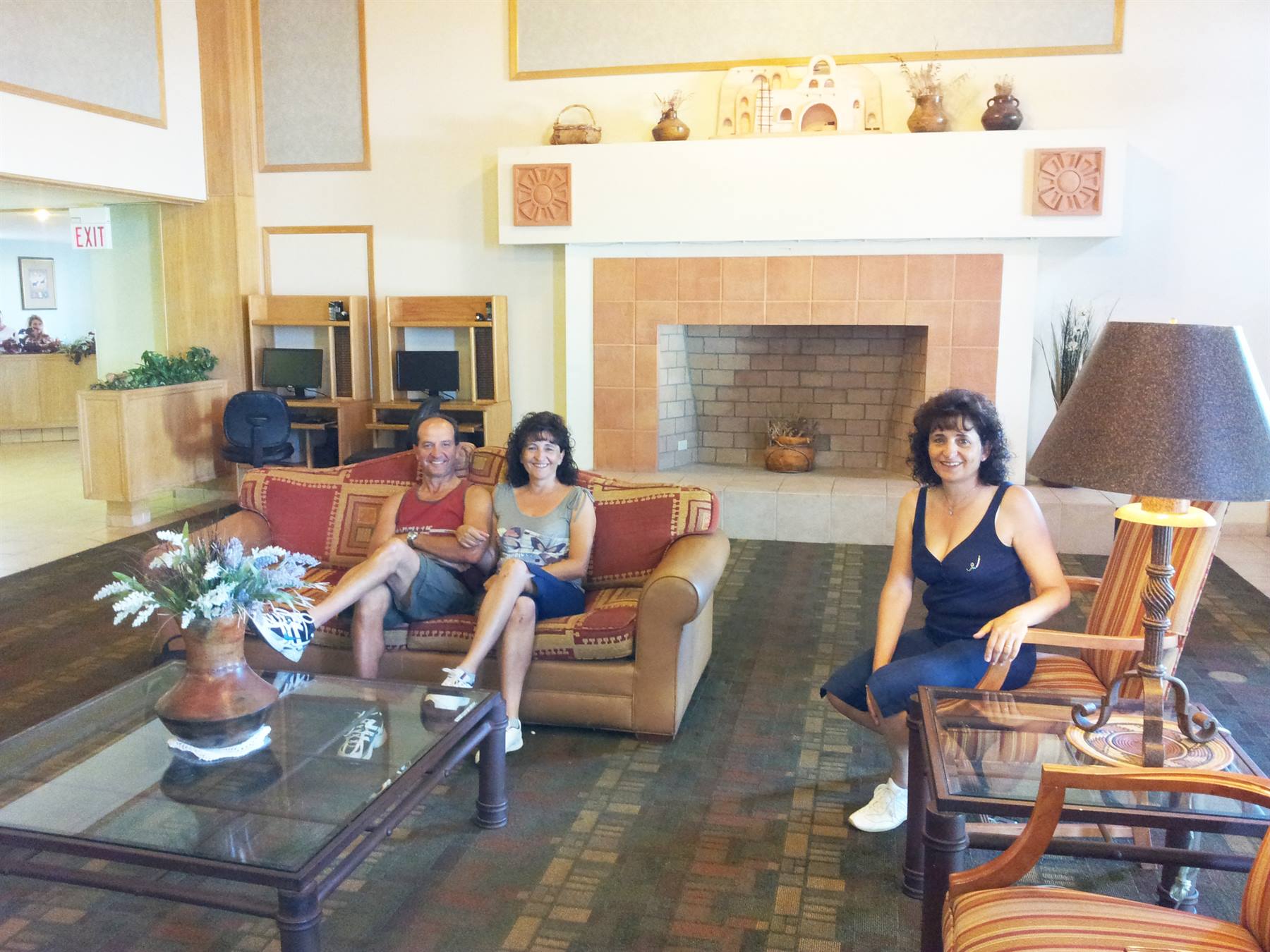 Three smiling people on sofas in a lobby with large fireplace and lamp