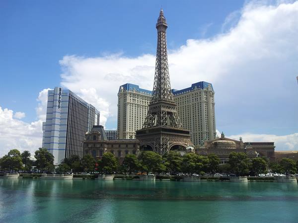 Steel Eiffel Tower replica behind hotels, green lagoon under cloudy sky
