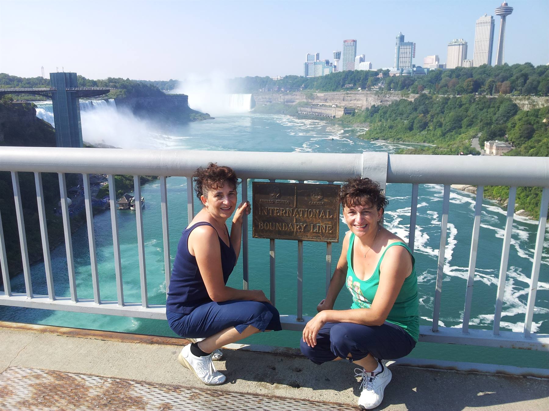Two women crouching by the International Boundary Line sign at Niagara Falls