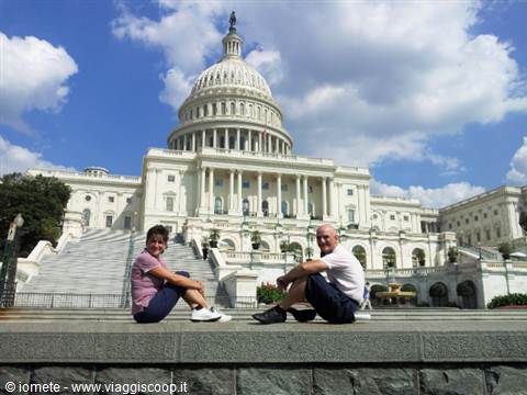 Two tourists sitting in front of the US Capitol, white marble and cloudy sky