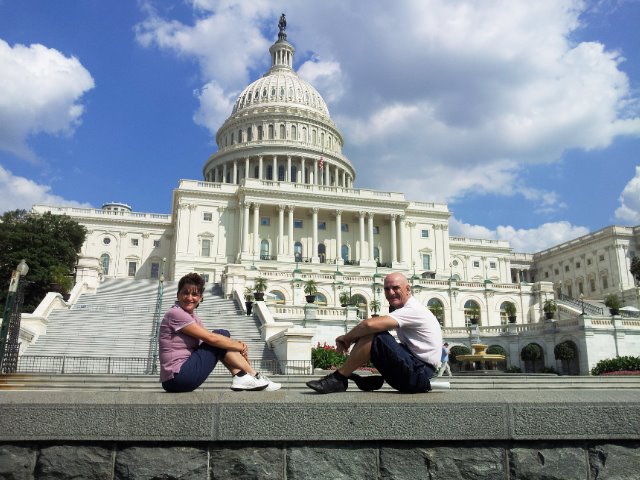 Two tourists sitting in front of the US Capitol, white marble and cloudy sky
