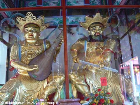 Golden guardian temple statues behind glass, one playing a pipa