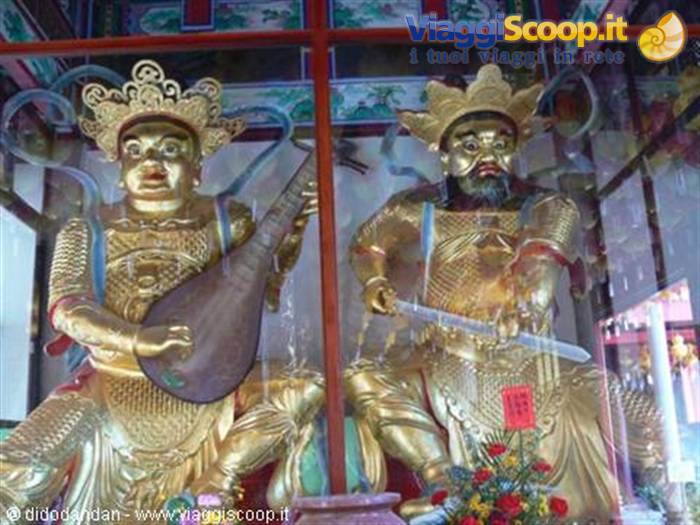 Golden guardian temple statues behind glass, one playing a pipa
