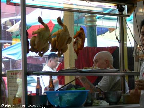 Roast chickens hanging at a street food stall, bald cook at work