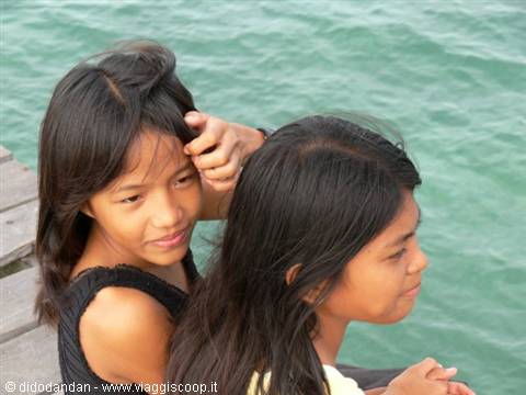 Two girls on a wooden pier gazing at the turquoise sea