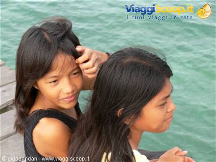 Two girls on a wooden pier gazing at the turquoise sea