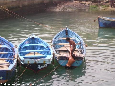 Two boys on moored blue boats in the harbor, Arabic writing on the wood