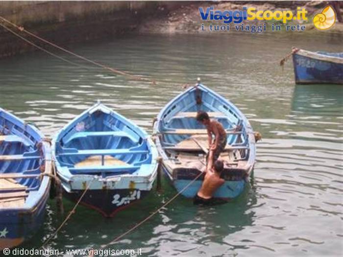 Two boys on moored blue boats in the harbor, Arabic writing on the wood
