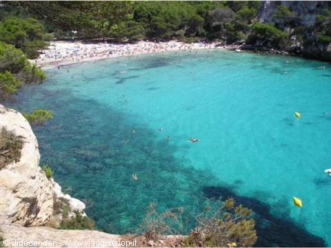 Swimmers in Cala Galdana's turquoise bay between white cliffs and pines