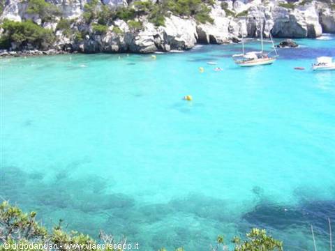 Sailboats anchored in a turquoise cove between white cliffs and pines